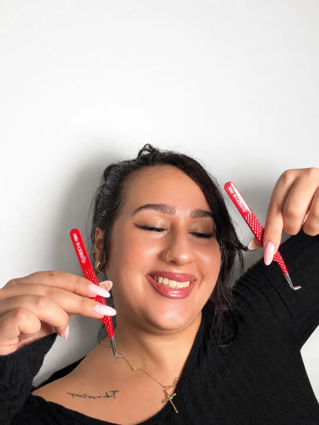 Anna smiling and holding two of her red Esthetics by Anna lash tweezers